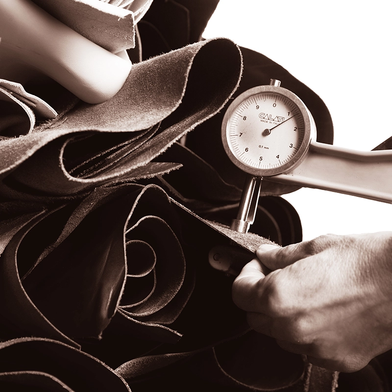 Hand misst die Dicke eines aufgerollten Lederstücks mit einem analogen Messgerät.